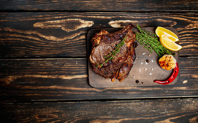 steak on a wooden board, lemon, red pepper, garlic and seasonings on a dark rustic background