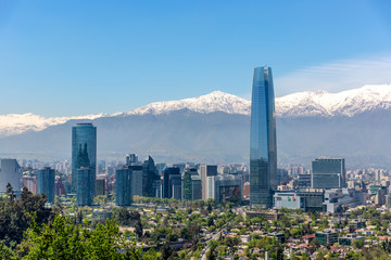 Plenty of business buildings in Santiago del Chile with trees in the foreground and the Andes mountains in the background