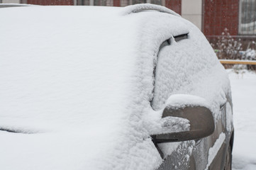 Fragment of a dirty car under a layer of snow during heavy snowfall, car is covered with snow, before snow cleaning