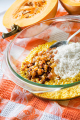 Raw washed millet, rice and raisins in a glass pan in the process of cooking milk pumpkin porridge