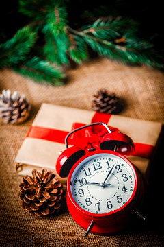 Christmas gift and pine cones with Alarm clock on jute background
