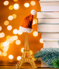 Christmas Santa Claus hat on Eiffel tower toy and pile of books with fairy lights on background