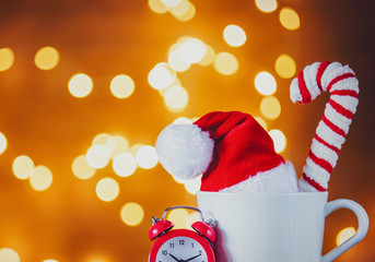 White cup of tea or coffee and alarm clock on Christmas Lights on background