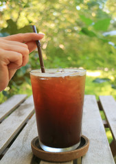 Female's Hand Holding a Straw in Iced Coffee Glass with Blurred Green Foliage in Background