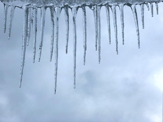 Winter background with melting icicles and cloudy sky