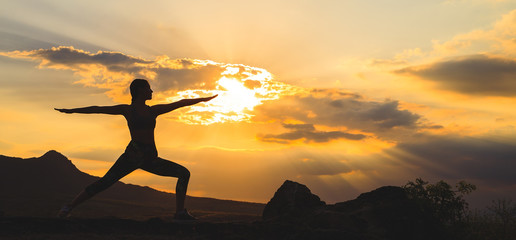 Silhouette of young woman practicing yoga or pilates at sunset or sunrise in beautiful mountain...