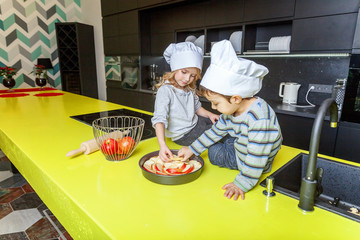 Little kids girl and boy with chef hat preparing bake homemade apple pie in kitchen. Brother and sister cooking healthy food at home and having fun. Childhood, household, teamwork helping concept