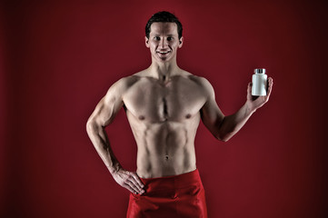 Man with strong belly hold pill jar. Red. Presenting product. Power and energy. Fitness and dieting concept. Sexy muscular man on red background. Anabolics and drugs for sport