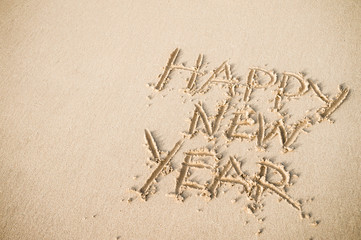 Happy New Year message handwritten on smooth sand beach