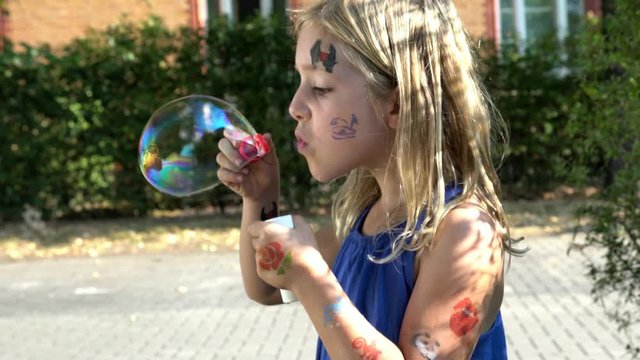 Little cute blond girl with painted face lets blow bubbles. Slow motion