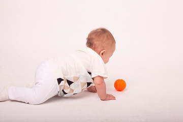 little baby playing with orange ball in white studio