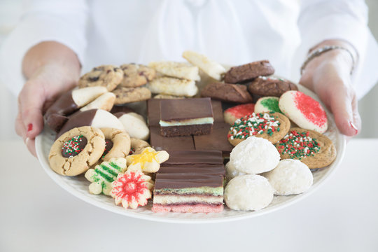 Christmas photograph of a woman's hands holding a platter of homemade Christmas cookies on white