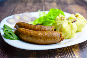 Sausages with green salad, balsamic vinegar, mashed potatoes, red onions, on a wooden rustic table. blur, clean, bright, authentic, retro, contrast, selective focus.