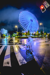 Ferris wheel with lights, reflections and cityscape at rainy night in Osaka Bay, Osaka, Japan