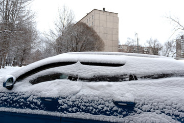 Blue car heavily covered with snow. Problem of snow removal