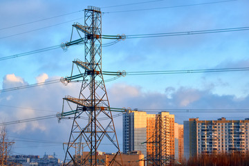 Supports of high-voltage power lines, modern houses, roads, Smoking pipes. In the foreground are trees without leaves, shrubs, and withered, autumn grass.