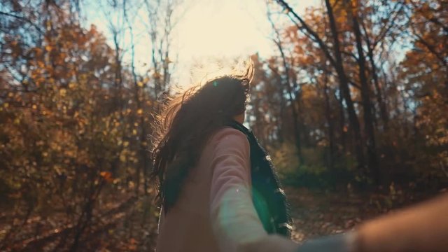 Cheerful woman is running in sunny fall day in park and stretching hand of her boyfriend. Man is filming her cute and joyful face and his hand in frame