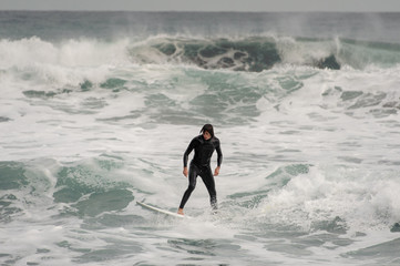 Brunette guy in the swimsuit professionally riding on a surf on the sea