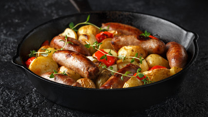 Homemade Pork sausages with potato, red pepper and onion in cast iron vintage pan.