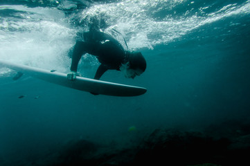 Man in the black swimsuit flowing down holding a surf board dive under the wave