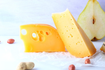 Various cheeses, pears and peanuts on white background. Blue cheese and camembert on parchment paper. Dairy products and fruits for breakfast. Healthy food. Copy space