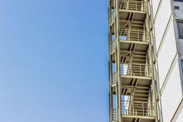 metal fire escape stairs construction outdoor side of high building and empty blue sky, copy space