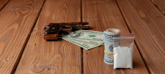 Stack of Money, drugsand a gun on a wooden table, concept about danger and threat of the drug