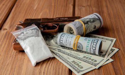 Stack of Money, drugsand a gun on a wooden table, concept about danger and threat of the drug