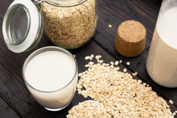 Glass of vegan, dairy-free oat milk and oats on a dark wooden background with texture. Concept of a vegan diet.