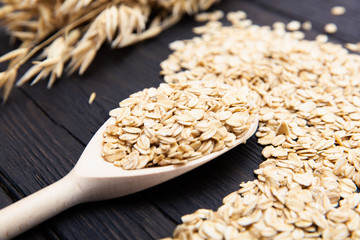 Rolled oats or oat flakes on wooden spoon on dark wooden background with texture. Healthy...