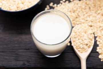 Glass of vegan, dairy-free oat milk and oats on a dark wooden background with texture. Concept of a vegan diet.