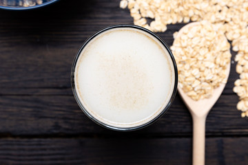 Glass of vegan, dairy-free oat milk and oats on a dark wooden background with texture. Concept of a vegan diet.
