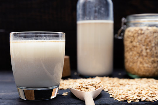 Glass of vegan, dairy-free oat milk and oats on a dark wooden background with texture. Concept of a vegan diet.