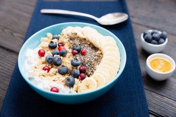 Healthy fitness breakfast: oatmeal with bananas, blueberries and cranberries, chia seeds and yogurt on dark wooden board with texture