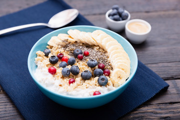 Healthy fitness breakfast: oatmeal with bananas, blueberries and cranberries, chia seeds and yogurt on dark wooden board with texture