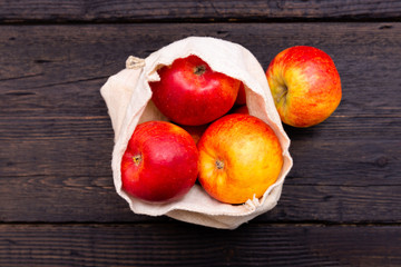 Zero waste grocery shopping. Package-free fruits on dark wooden table with texture. Fresh apples in Eco cotton bags. Plastic-free package