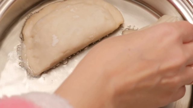 Close-up. Female hand puts raw pasties chebureks in the pan with hot oil. Cooking fried meat pie.