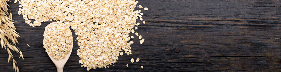 Rolled oats or oat flakes on wooden spoon on dark wooden background with texture. Healthy...