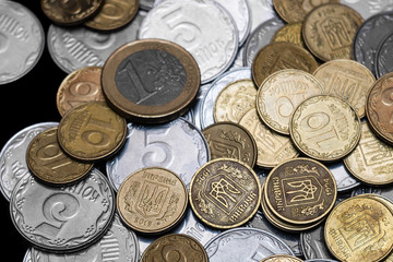 Ukrainian coins with one euro coin isolated on black background. Close-up view. Coins are located at center of frame. A conceptual image.