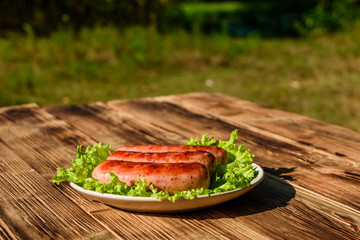 Ceramic plate with grilled sausages and lettuce leaves on wooden table