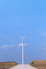 Fototapeta na wymiar One single windmill turbine in front of road with blue sky in background. Renewable energy wind turbine