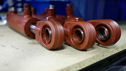 Three brown hydraulic cylinders lie in a row on a wooden surface