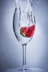 Strawberry splash plunge into water in a wine glass. 