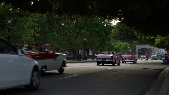 Row of 1950's American vintage classic  convertible cars driving on old street Vieja neighborhood Havana, Cuba