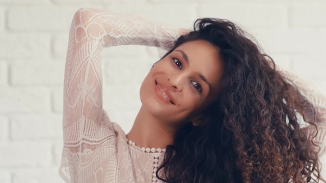 Portrait of beautiful young woman with curly hair on a white wall, 4k 75 fps slow motion