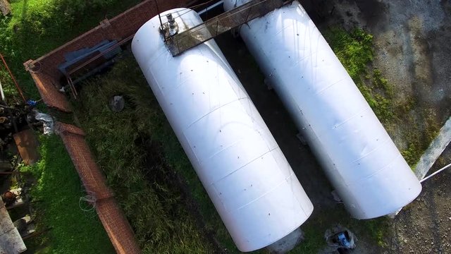 Top view of big silver cisterns, petroleum reservoir at oil storage depot on green grass background. Stock. Aerial top view for fuel tanks in industrial zone.