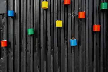 many painted colorful empty cans reused as flower pots, mounted to the black metal wall