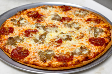 Sausage and pepperoni pizza fresh out of the oven.  Not cut.  Whole pizza on pan.  Prepared in a restaurant.