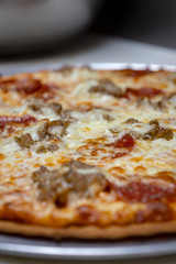 Close up side view of sausage and pepperoni pizza fresh out of the oven.  Blurred background.  Portrait view.  Prepared in a restaurant.