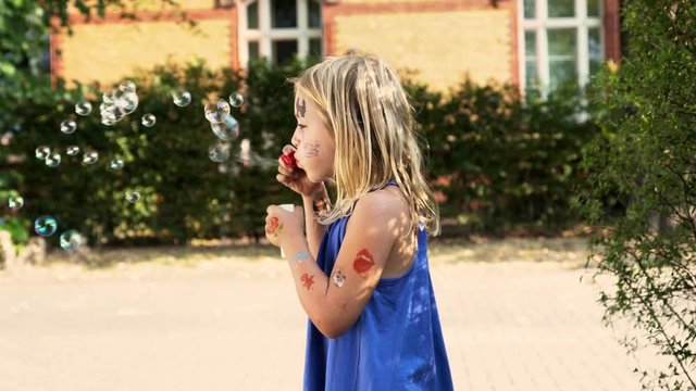 Little cute blond girl with painted face lets blow bubbles. Slow motion